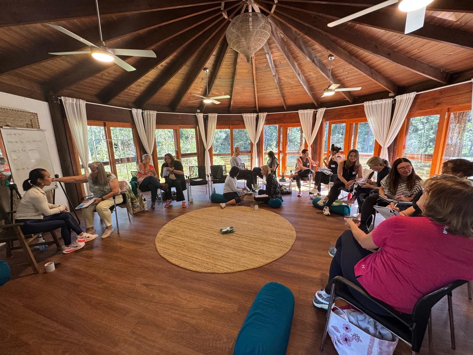 Workshop participants seated in a large circle in a circular timber pavilion with panoramic forest windows