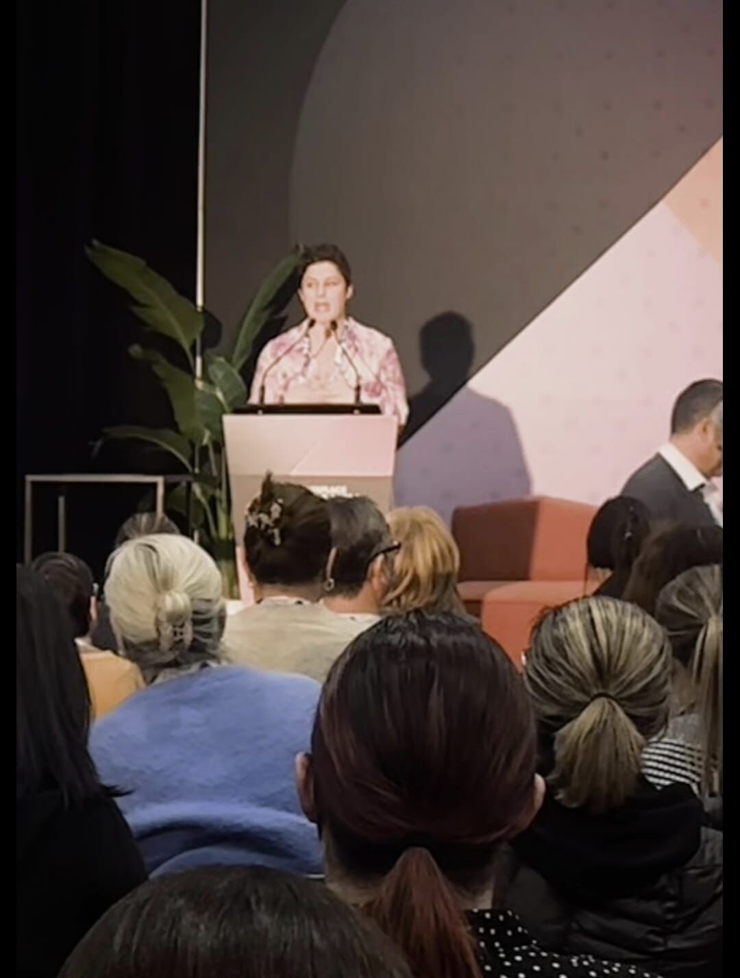 Amanda Anderson at a mental health conference podium, speaking to a full, attentive audience