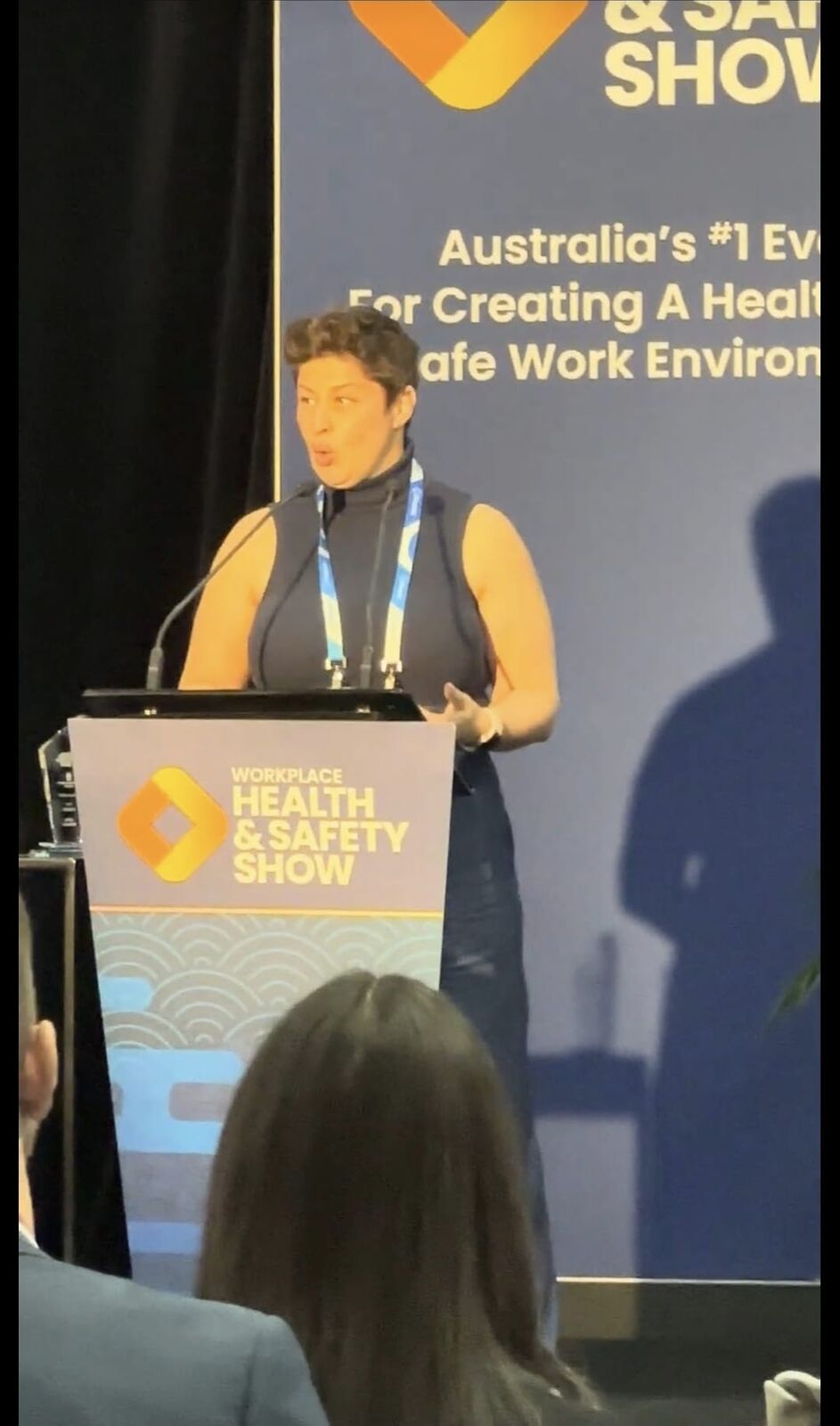 Amanda Anderson speaking at the Workplace Health & Safety Show podium — close-up portrait mid-speech